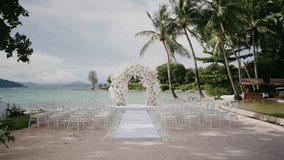 Romantic beach wedding setup with white floral arch, aisle, and chairs under palm trees by turquoise sea, perfect for destination weddings and tropical ceremonies. - Powered by Shutterstock - Get 15% off with code: PIKWIZARD15