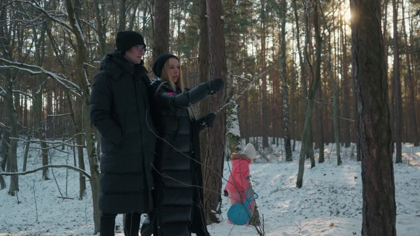 Happy family having fun while sledding in a winter forest. Parents watch their children as the kids slide down a snowy hill on sleds, enjoying outdoor recreation on a beautiful cold day.