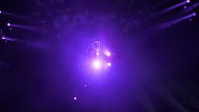 A slender aerial gymnast quickly rotates around herself on a gymnastic hoop under the dome of the circus. Aerial gymnast's performance, a cannon with smoke on the front panel. Circus show. - Powered by Shutterstock - Get 15% off with code: PIKWIZARD15