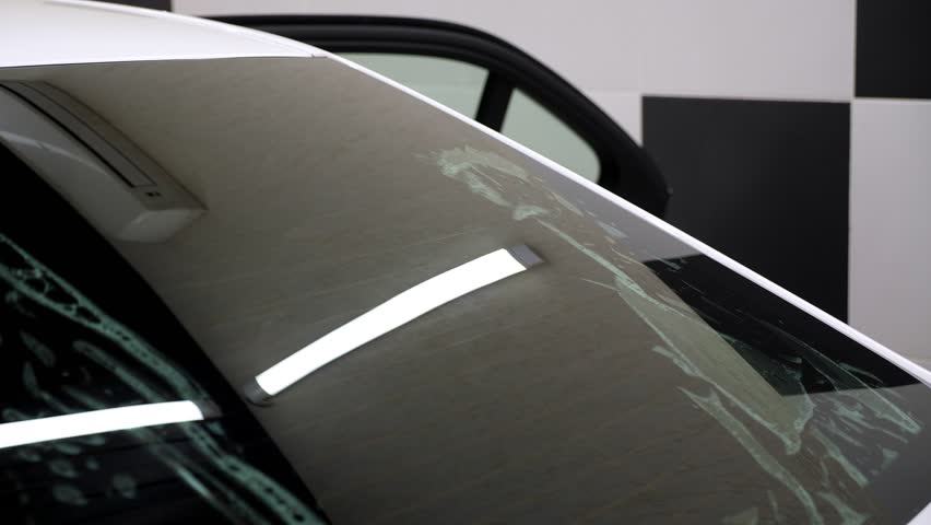 A close-up of the car servicemaster glues the tinting film on the glass, he smoothes the foil with a spatula. The process of tinting a car in a car service.