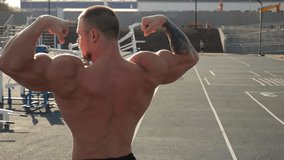 A handsome, muscular man shows off a toned back and arms. A bodybuilder shows off a toned body on an outdoor sports field at sunset. Outdoor exercise equipment. The image is stabilized. - Powered by Shutterstock - Get 15% off with code: PIKWIZARD15