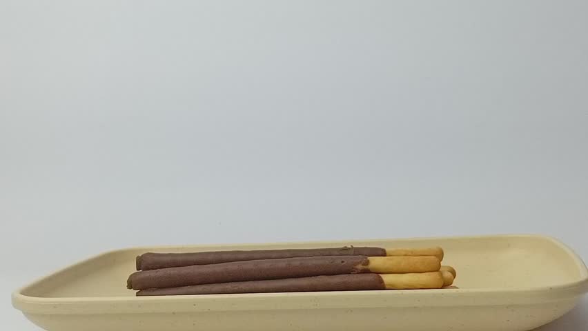 Hand pick up chocolate biscuit stick on a square plate, isolated on white background.