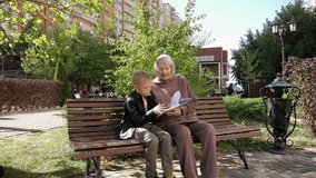 An elderly woman with gray hair and her grandson are reading a book together in the park on a bench, the grandson spends time with an old grandmother. Stable image. - Powered by Shutterstock - Get 15% off with code: PIKWIZARD15