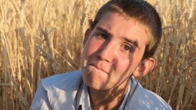 Very cute Caucasian teenage boy with brown eyes and short hair making funny faces and smiling while sitting in a wheat field. Interesting young man in a shirt outdoors. Attractive teen - Powered by Shutterstock - Get 15% off with code: PIKWIZARD15