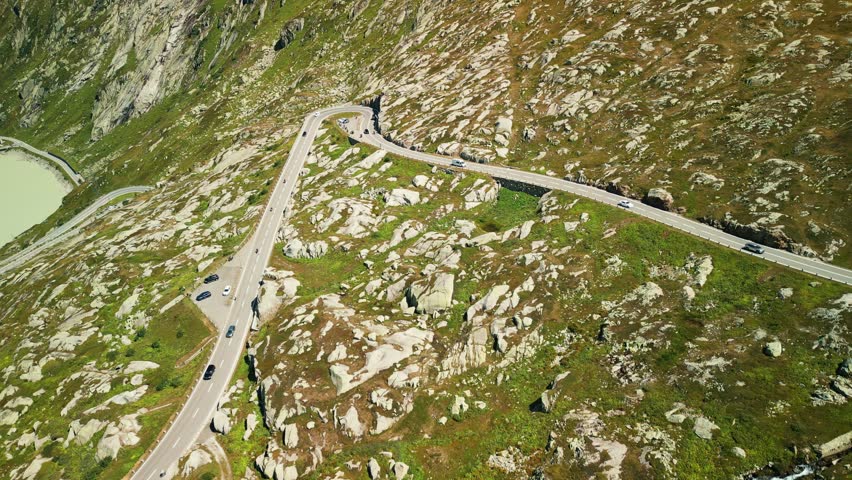 Alpine car road on Grimsel mountain pass in Switzerland Alps mountains. Car driving along winding asphalt road through mountain pass with lake