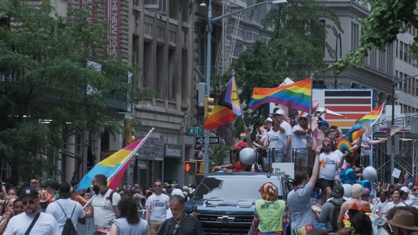 New York, NY USA June 29 2025: People marching in a Pride parade wearing “I Stand Proud” shirts and holding Progress Pride flags. Public event celebrating LGBTQ+ rights and inclusivity.