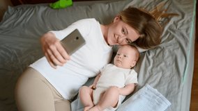 Happy cute mother and baby in bed, looking at mobile phone camera, taking selfie. Young family communication online, video call, technology, communication concept. - Powered by Shutterstock - Get 15% off with code: PIKWIZARD15
