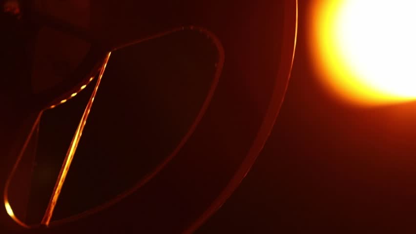 Close-up of a vintage film reel spinning, bathed in a warm, orange glow with beautiful light flares. Evokes nostalgia for classic cinema and movie projection. Perfect for film history, entertainment.