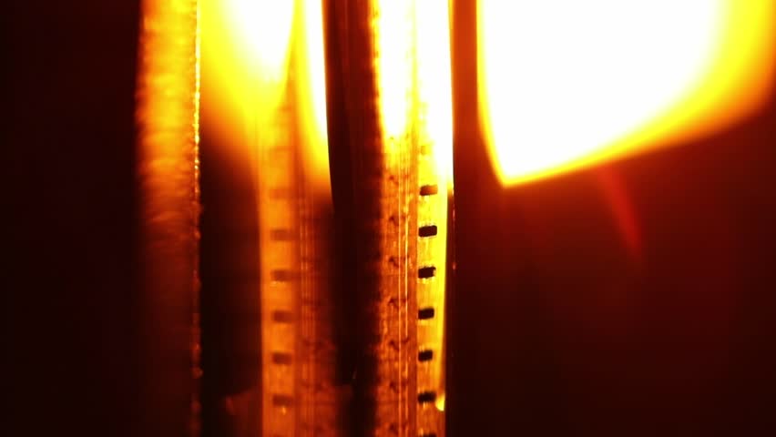 Close-up of a vintage film reel spinning, bathed in a warm, orange glow with beautiful light flares. Evokes nostalgia for classic cinema and movie projection. Perfect for film history, entertainment.
