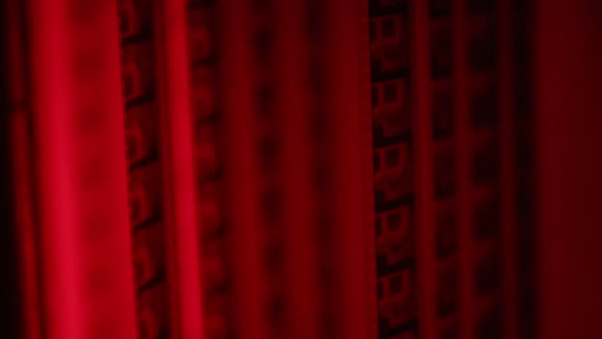 Dramatic close-up of a vintage film reel rotating and unwinding, bathed in striking red light. Perfect for cinematic, nostalgic, or artistic projects, evoking classic movie themes and atmosphere.