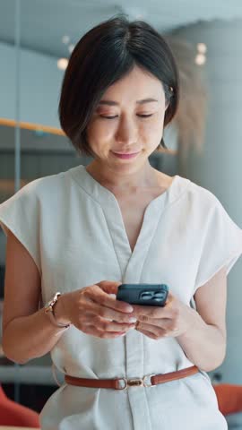 Asian mature business woman manager ceo using cell phone mobile app. Smiling eastern 40s female businesswoman holding smartphone in office workspace for trading, banking, working online. Vertical