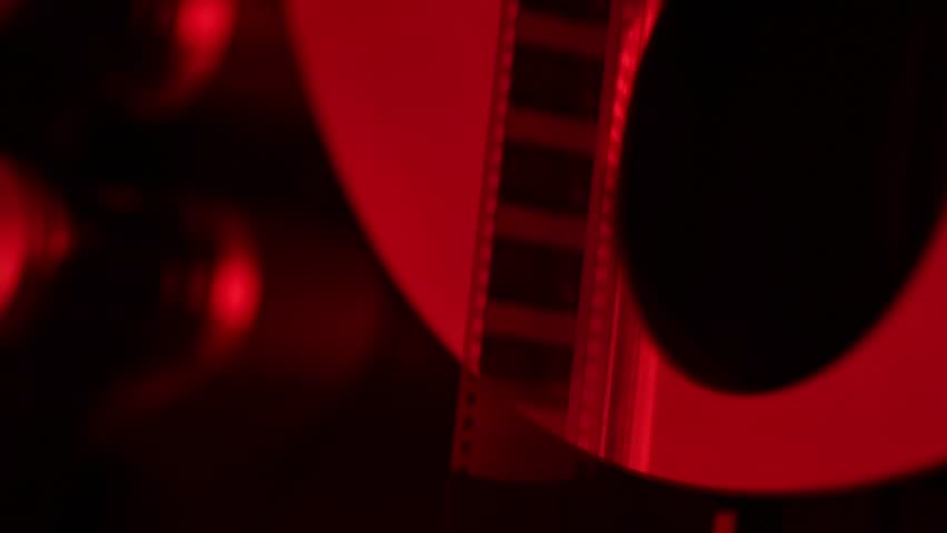 Dramatic close-up of a vintage film reel rotating and unwinding, bathed in striking red light. Perfect for cinematic, nostalgic, or artistic projects, evoking classic movie themes and atmosphere.