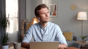 Thoughtful elegant man working online on laptop wearing wireless headphones. Attractive busy male using technologies working from home in living room. Working online concept. - Powered by Shutterstock - Get 15% off with code: PIKWIZARD15