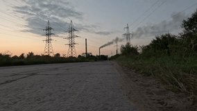 Static 4K 60fps video of high voltage transmission towers and electric power lines with a factory chimney emitting smoke in the distance during sunset. Industrial landscape, energy production, and env - Powered by Shutterstock - Get 15% off with code: PIKWIZARD15