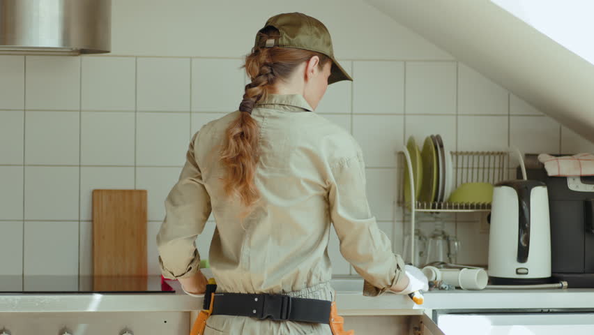 A plumber smiles brightly, holding a wrench in a modern kitchen. Cheerful and competent service for home repair and maintenance.