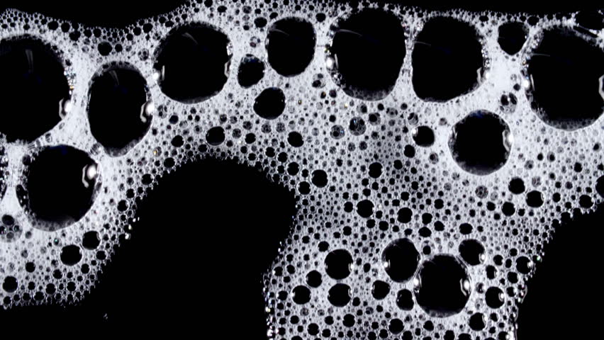 Bubbles of white soap foam. Moving Soap foam popping bubble on a black backdrop. Soap sud macro structure. Clean, cleaning concept, laundry, shower. 