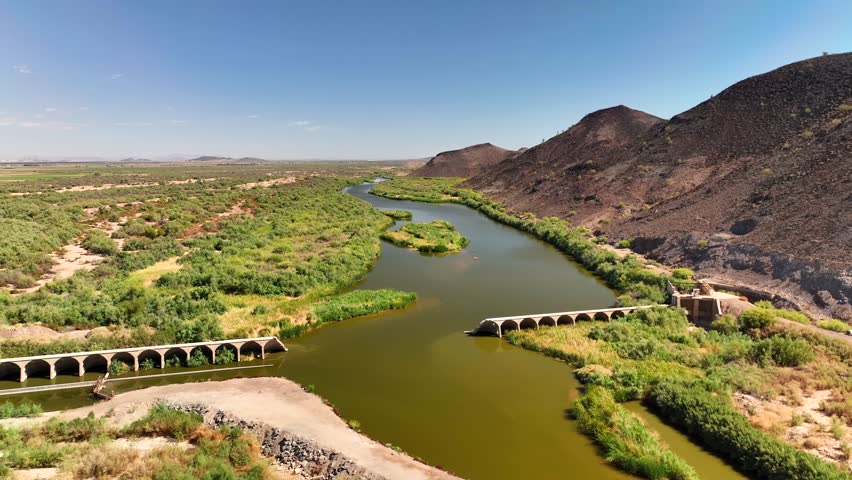 Aerial view of the Gila River winding through a landscape, with bridges spanning its waters, and arid terrain meeting lush riverbanks, Arlington, Arizona, United States.