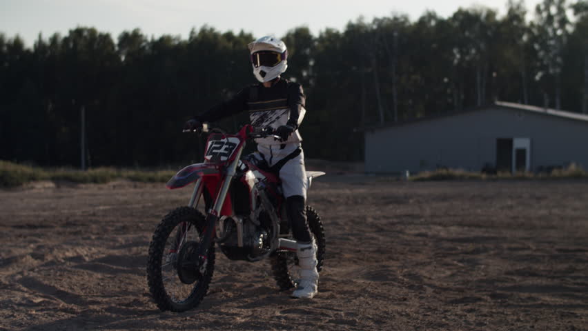 Moto crosser in protective suit and helmet sits on motorcycle