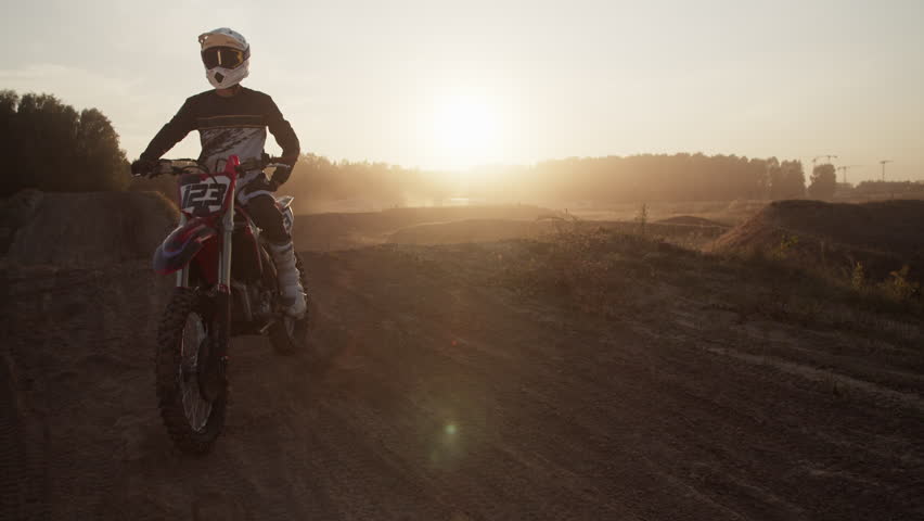 Skilled motocrosser in protective costume rests on motorcycle