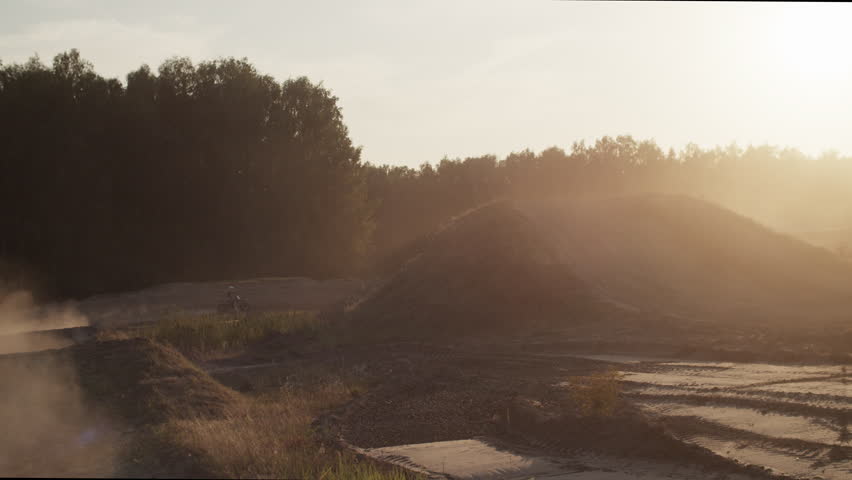 Dark silhouette of motorcyclist jumping on motorbike over hills