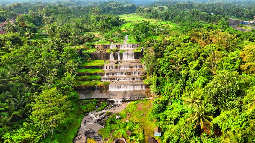 A stunning tiered waterfall cascading gracefully over stone steps, surrounded by lush tropical greenery and clear flowing water, located in Grojogan Watu Purbo Sleman Yogyakarta Indonesia.