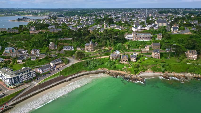 Plage de Trestignel beach and Perros-Guirec coastal town, historic houses on green hills, Brittany, France. Aerial drone forward
