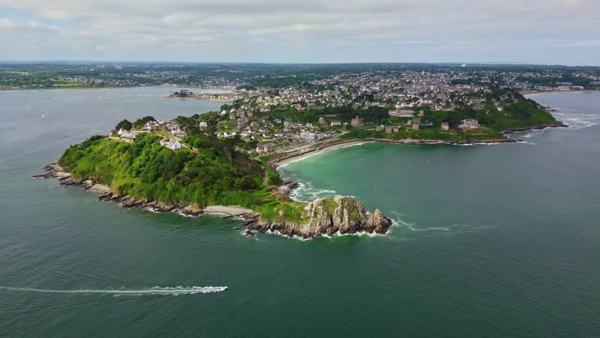 Perros-Guirec coastal town, Pointe du Chateau headland, Plage de Trestignel beach, and houses on green hills, Brittany, France. Aerial drone forward