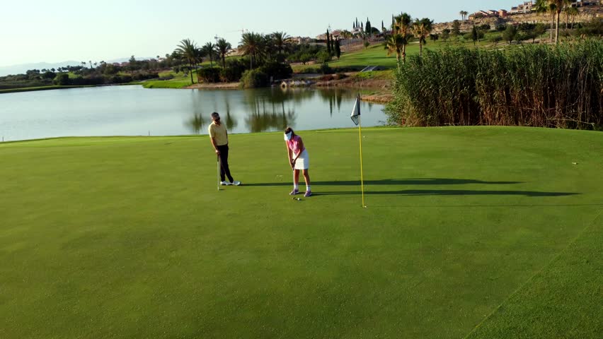 Professional golf instructor providing detailed putting guidance to student on scenic resort green near tranquil lake during golden sunset hours - Powered by Shutterstock - Get 15% off with code: PIKWIZARD15