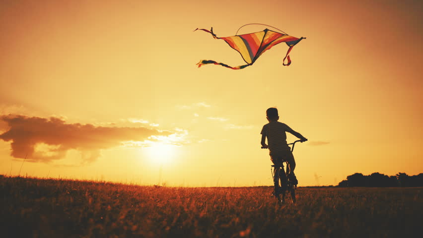 Carefree childhood, little boy spending summer vacation in country, riding bike. Slow motion shot with flying kite and silhouette of child riding bicycle, merry weekend, children games outdoors