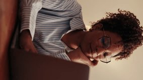Vertical video,Happy young woman working from home on her laptop. She's wearing glasses and a striped shirt and looks thoughtful while working. - Powered by Shutterstock - Get 15% off with code: PIKWIZARD15