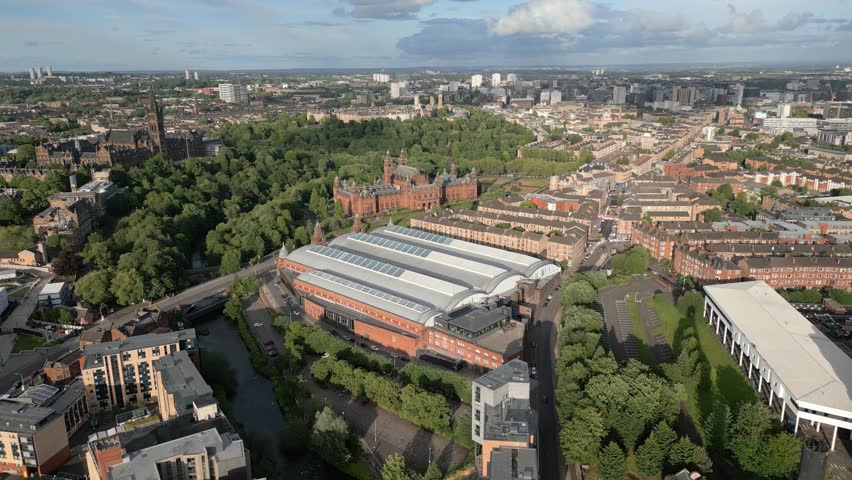 Aerial fly towards Kelvin Hall museum in natural parkland with Kelvingrove Art Gallery and Museum in background, Glasgow, Scotland, UK