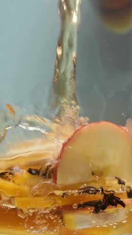 Hot water pours over black tea with apple, ginger and lemon, brewing vitamin rich infusion in clear glass, close-up shot.