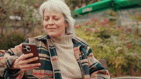 Smiling senior woman using smartphone outdoors. An elderly lady browsing internet, social media, or ecommerce on mobile phone in a park. - Powered by Shutterstock - Get 15% off with code: PIKWIZARD15