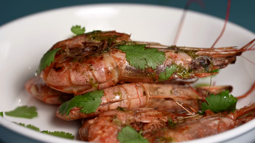 Close-up of grilled whole shrimp covered in green herb sauce, garnished with fresh cilantro leaves.