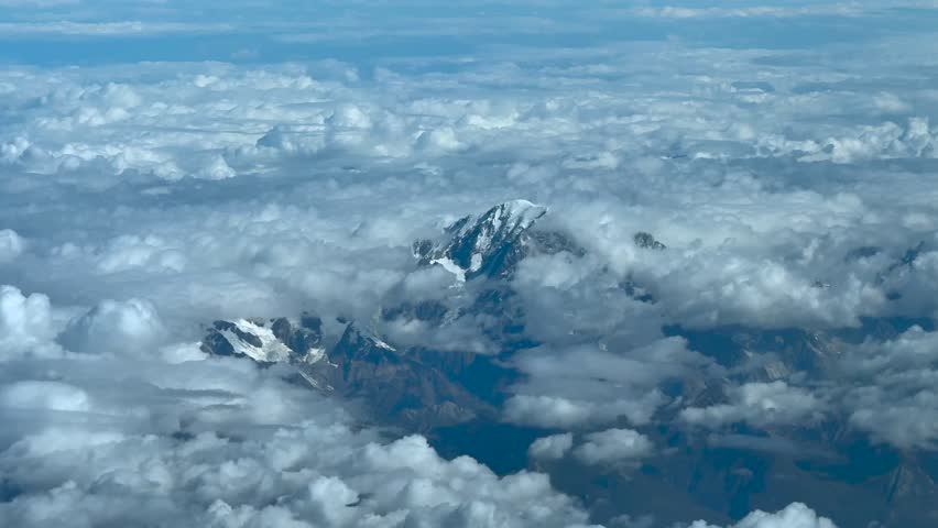 An elevated aerial view taken from a jet cockpit flying near the summit of the Mont Blanc, with few snow, in a summer morning, surroended by cottony clouds.