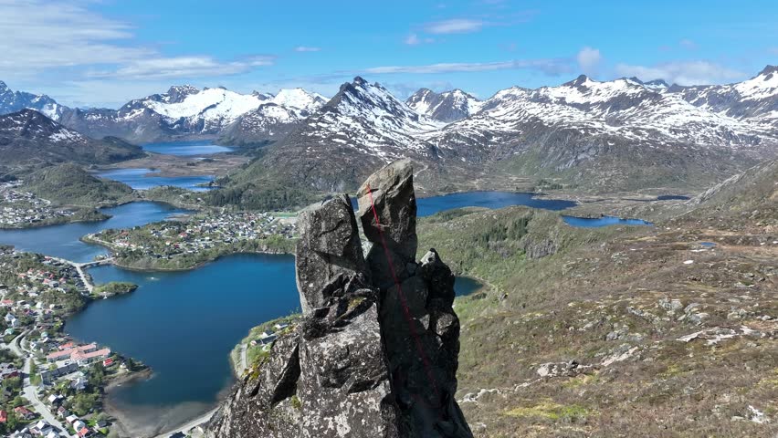 Drone glides past the horns of Svolvaergeita in Lofoten, showing climbing rope and parallax view of Svolvaer