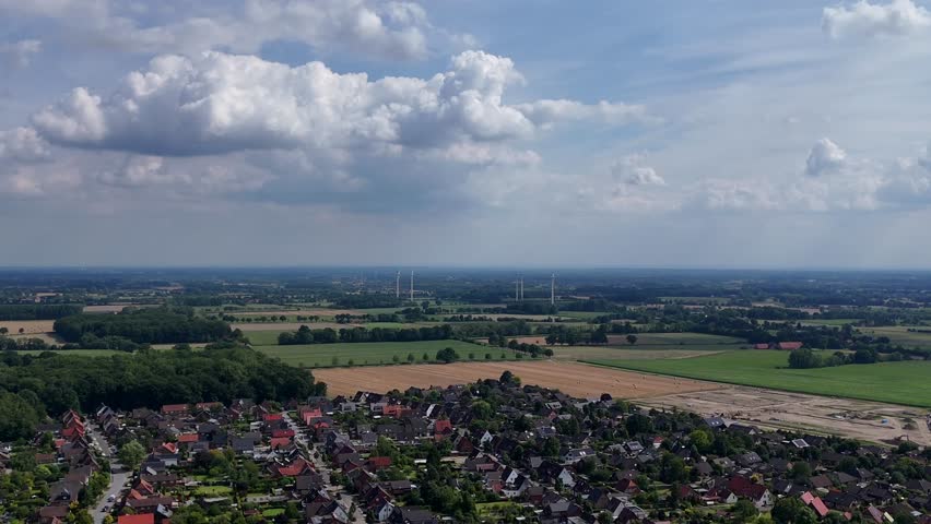 Quiet rural neighborhood of USA with wind turbines on agricultural farm fields. Aerial wide shot. Puffy clouds at sky. Houses and homes of small American town. Summer day season