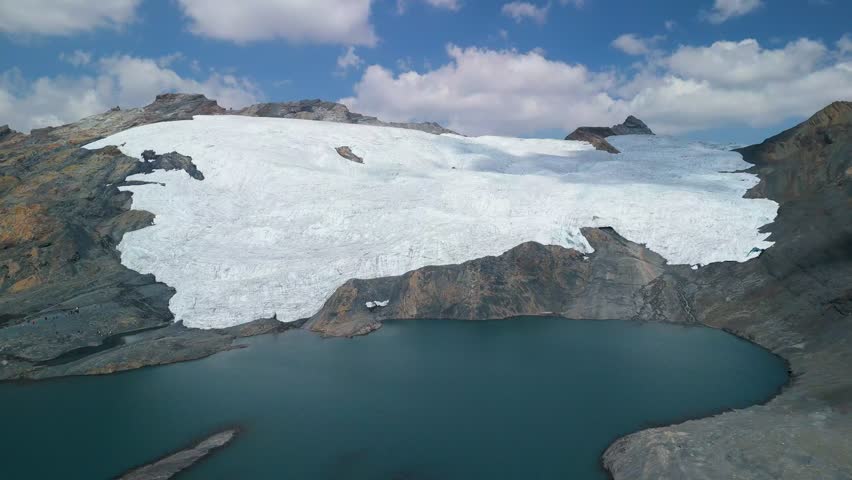 A stunning forward-moving aerial drone shot flies over the vast, icy expanse of the rapidly receding Pastoruri Glacier in the high Andes of Huascarán National Park, Peru.