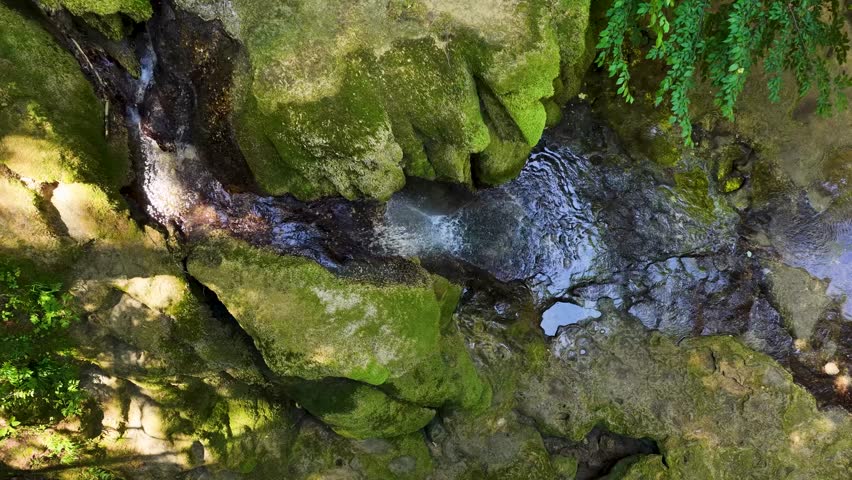 Overhead perspective of a small cascading waterfall, camera tracking gently from left to right