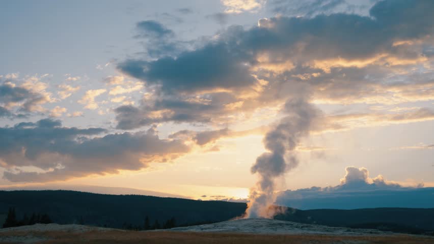 Old Faithful geyser in Yellowstone erupting at sunset.