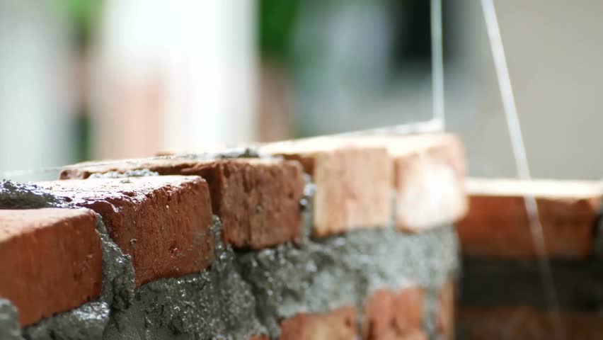 Skilled hands position bricks and apply mortar to build a durable wall. The setting features natural light illuminating the brickwork, highlighting craftsmanship in progress.