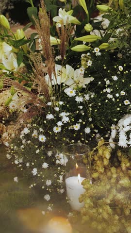 Vertical video. Candles burning surrounded by flowers. Close-up of wedding floral decor on the floor in retro style, beautiful floral arrangements for a wedding with candles and moss.