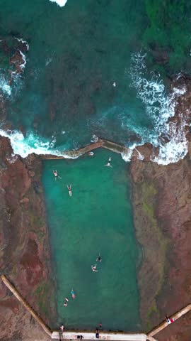 Aerial view of people enjoying the tranquil turquoise water of a natural pool surrounded by rocky terrain, Newcastle, nsw, Australia.