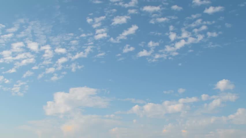 Small white clouds slowly floating across the blue sky. Background with a calm summer sky.