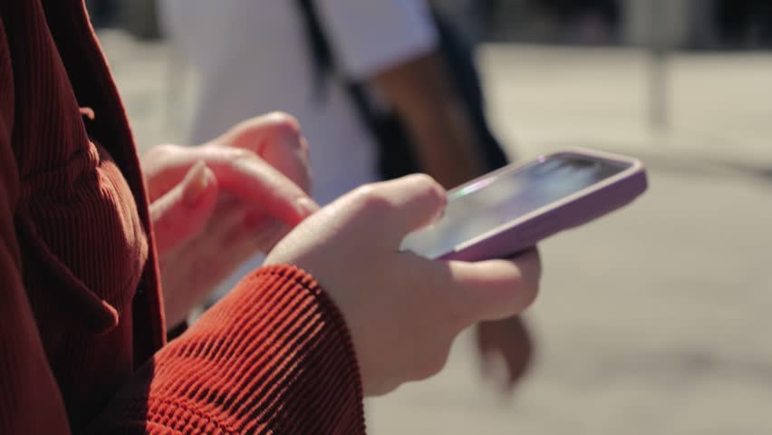 Person using smart phone outdoor, close up hands holding phone, woman walking with cell phone on city street. High quality 4k footage