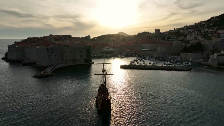 Aerial: old town of Dubrovnik with Adriatic Sea and a boat at sunset in southern Dalmatia, Croatia, orbit drone shot