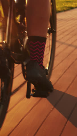Bike wheel rotation in sunset light. Woman riding bike at sunrise, close up of bike gear and legs. Cyclist training on bicycle on cycle path at sunset. Vertical video