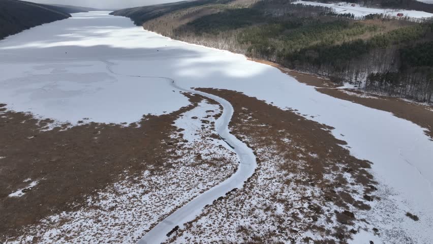 New York Hemlock Finger Lake Glacier Lake in winter frozen with snow as cloud shadows cross over surface ideal for ice fishing with frozen wetland marsh 