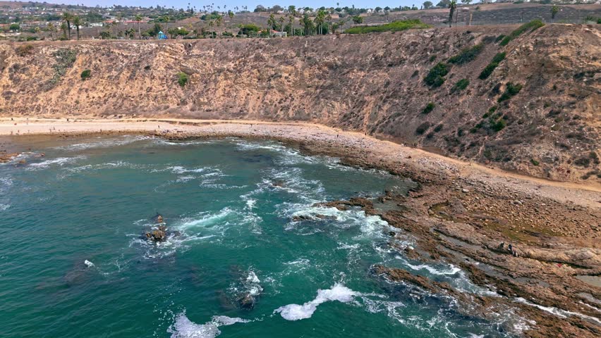 Low aerial push in shot of White Point Beach, Los Angeles, California on a sunny day with dramatic cliffs and waves crashing into the rocky beach