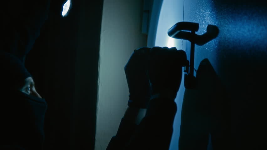 Professional hands of unrecognizable thief picking door lock while his accomplice illuminating door with flashlight